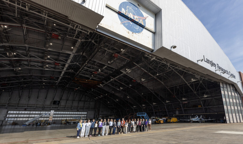 Purdue women students stand in the shadow of the entrance to NASA Langley's gigantic aircraft hangar.